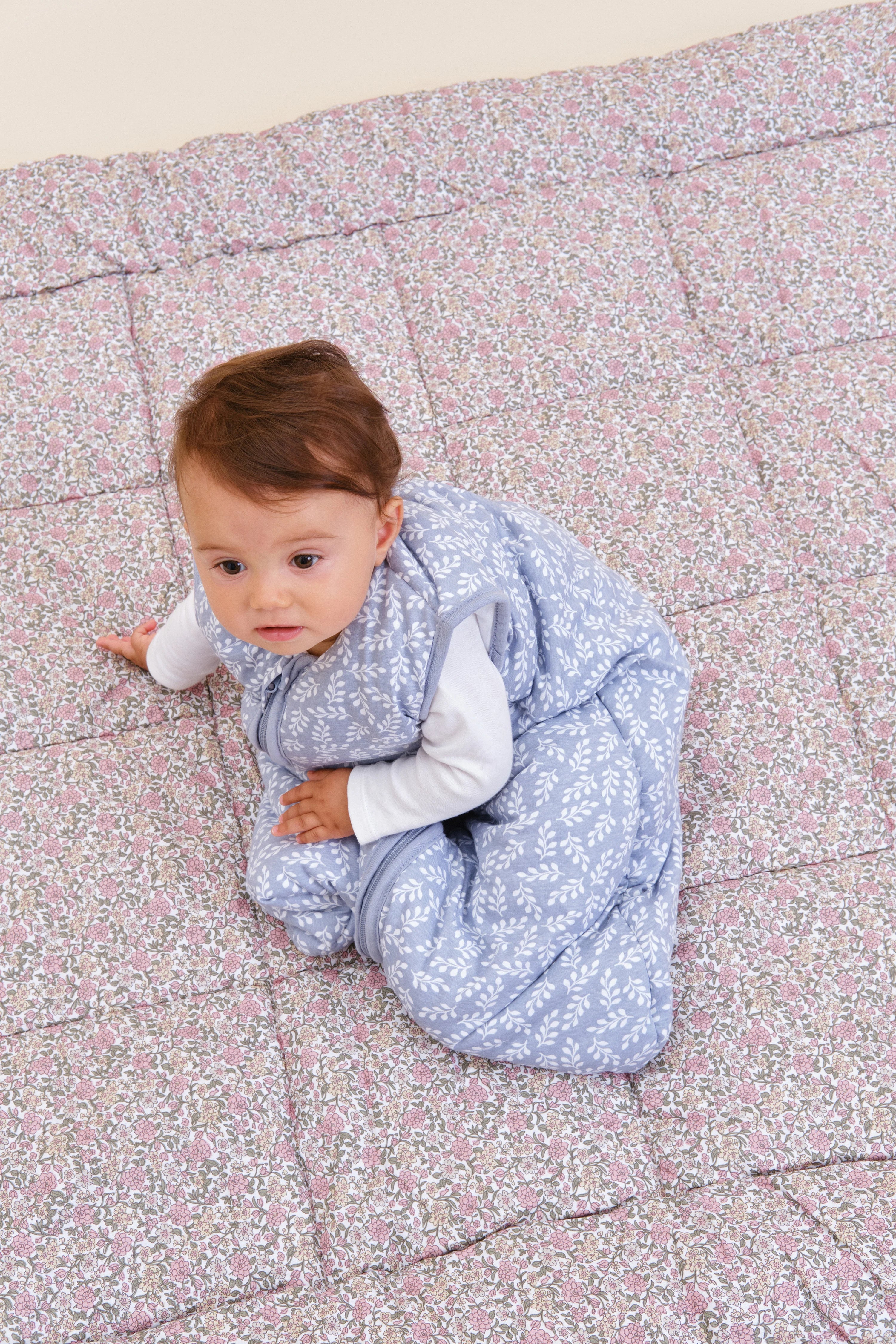 Bebé sentado no saco de dormir MolisandCo TOG 2.5 Blue Garden, demonstrando liberdade de movimento e design.