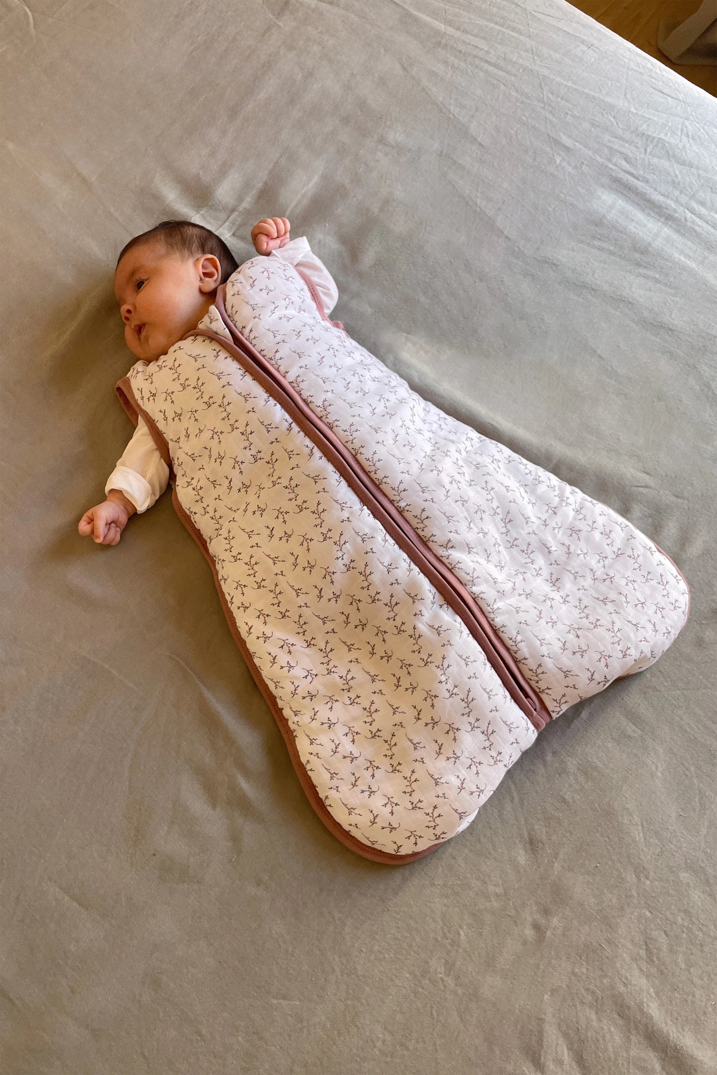 Bebé deitado na cama, a usar o saco de dormir MolisandCo TOG 2.5 em musselina de algodão rosa floral.