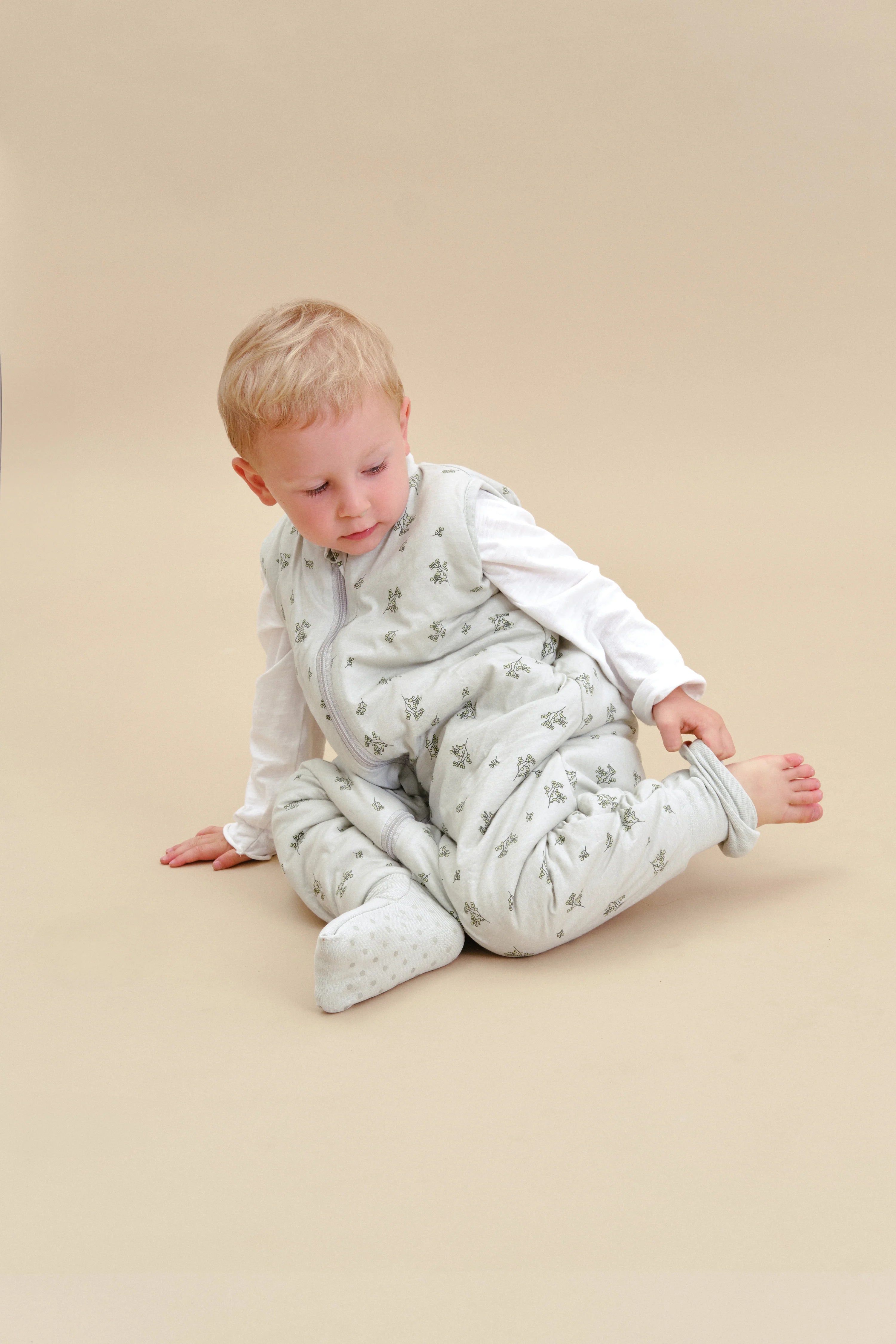 Criança sentada a ajustar a meia antiderrapante do saco de dormir MolisandCo TOG 2.5 com pés Botany Green, segurança e conforto.