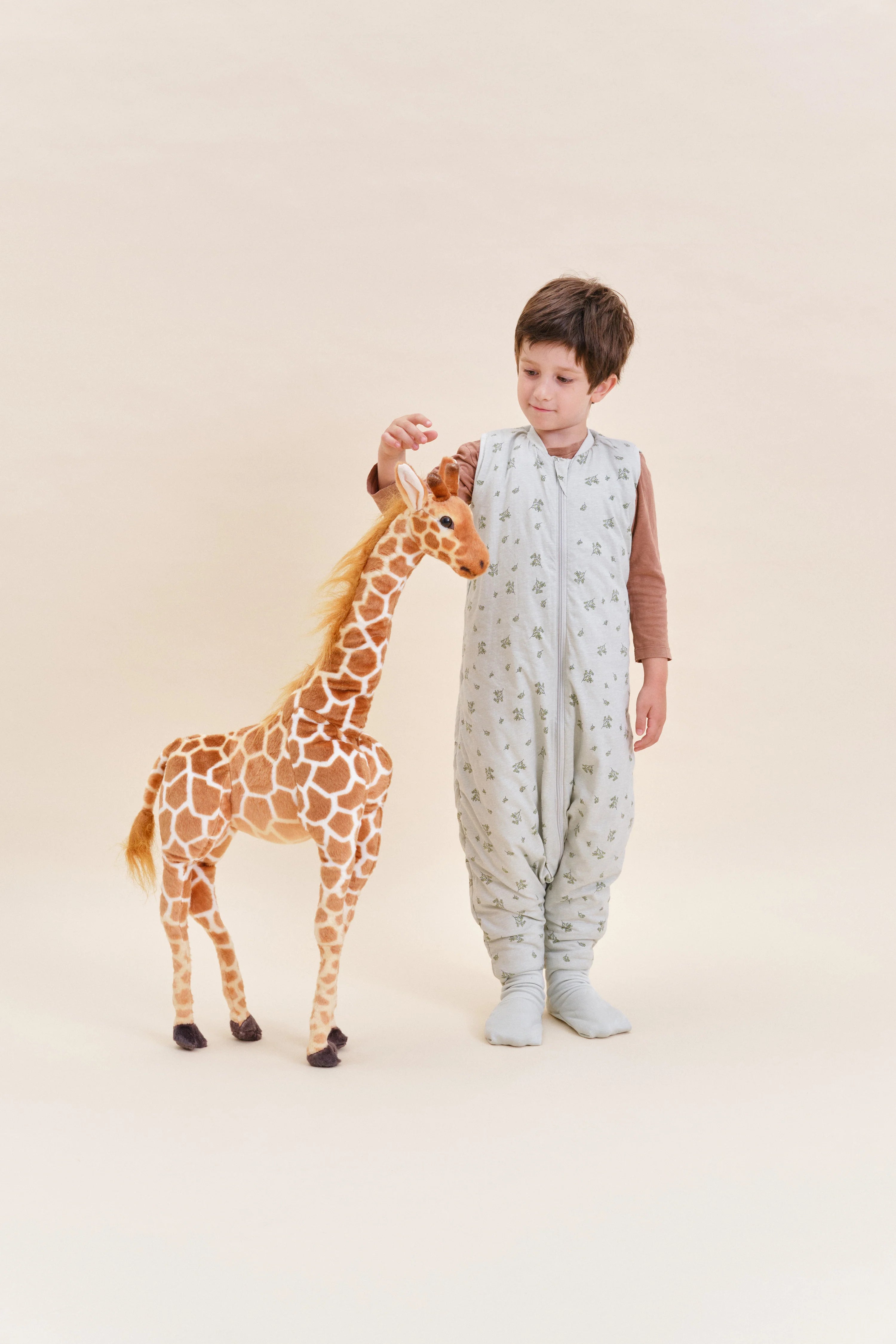 Menino a brincar com girafa de peluche, usando saco de dormir MolisandCo TOG 2.5 com pés Botany Green, realçando a mobilidade.