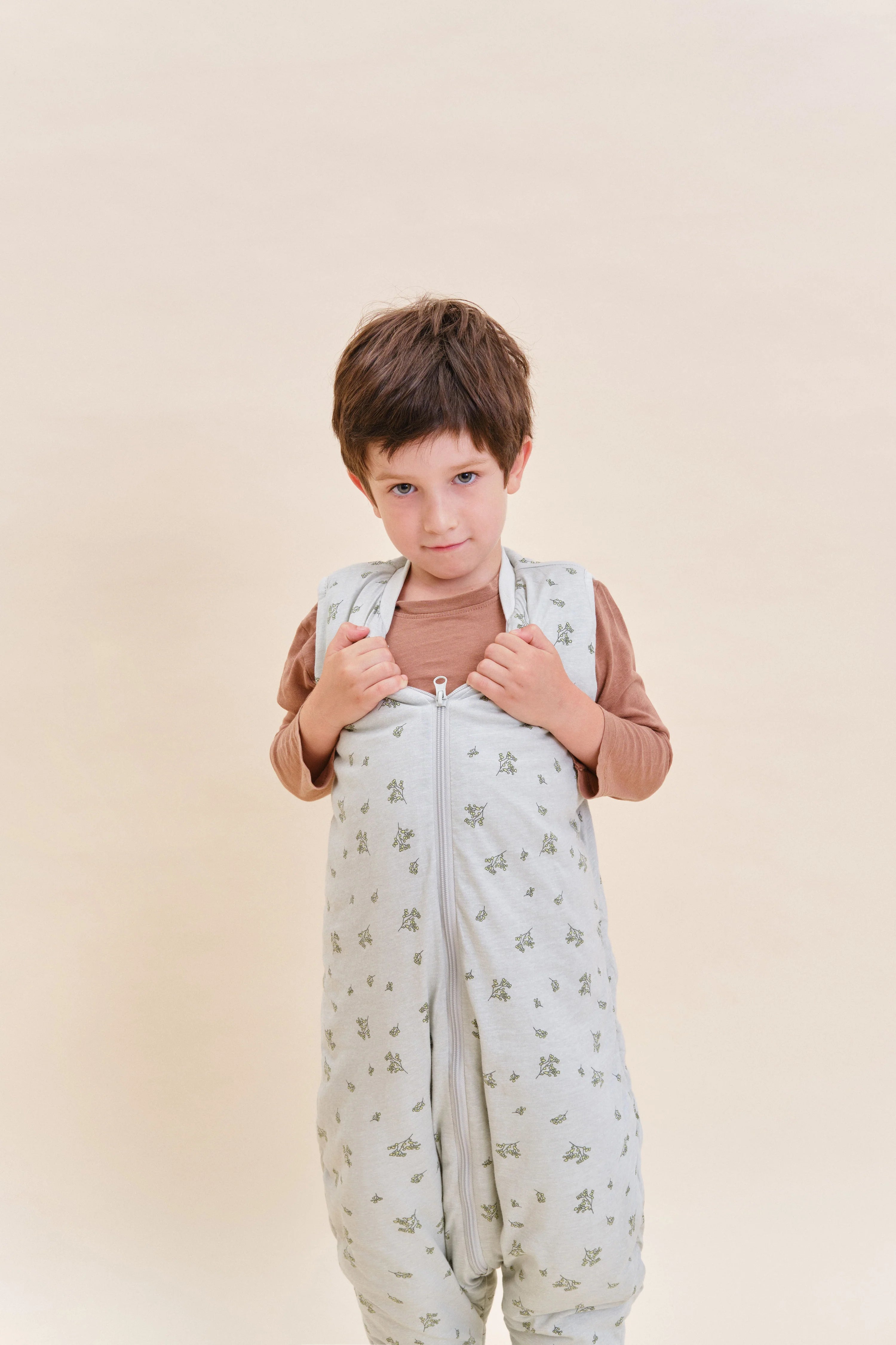 Menino a vestir saco de dormir MolisandCo TOG 2.5 com pés Botany Green, destacando o fecho frontal e o design confortável.