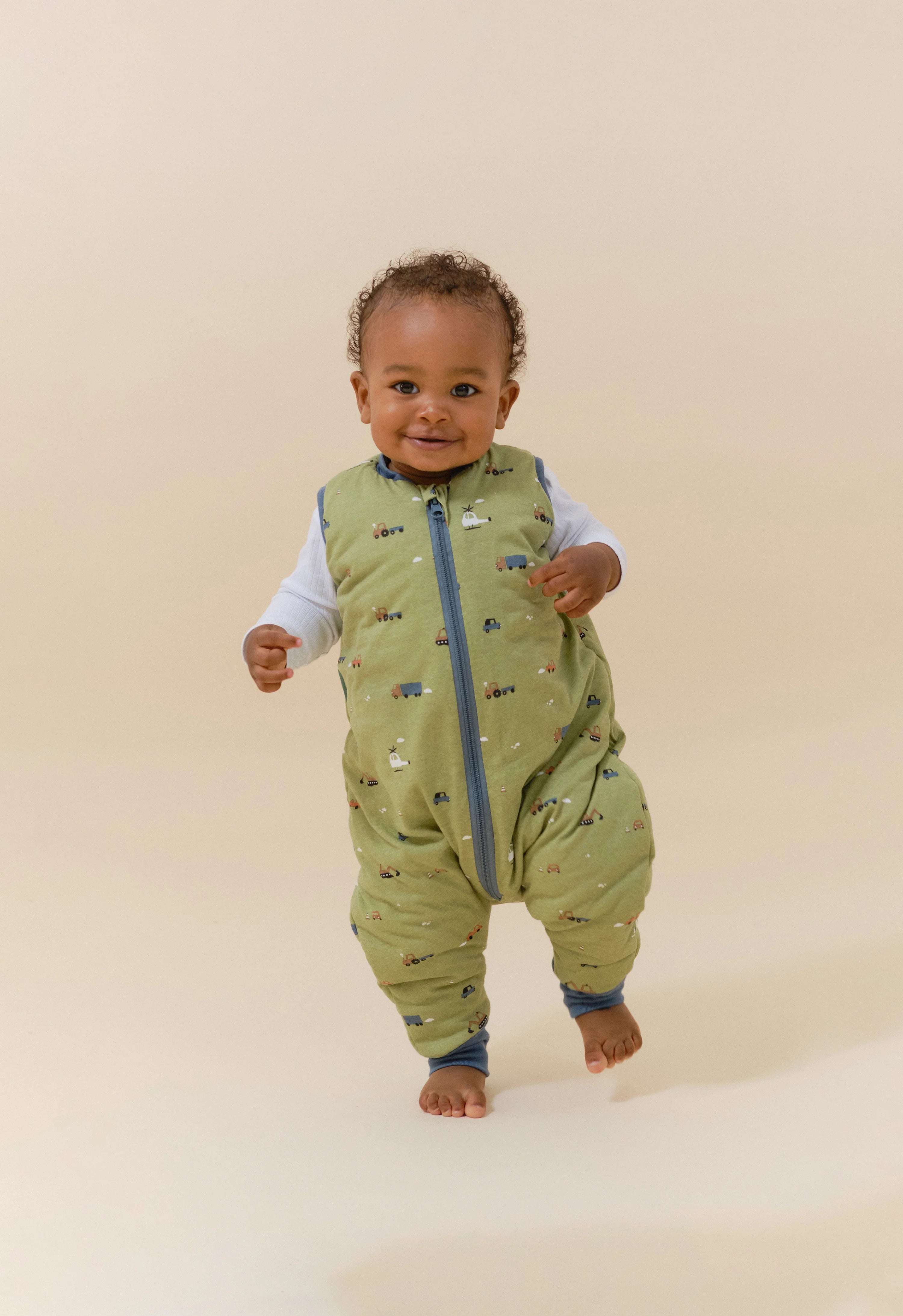 Bebé sorridente a caminhar com o saco de dormir MolisandCo TOG 2.5 com pés, padrão Little Drivers, liberdade total.