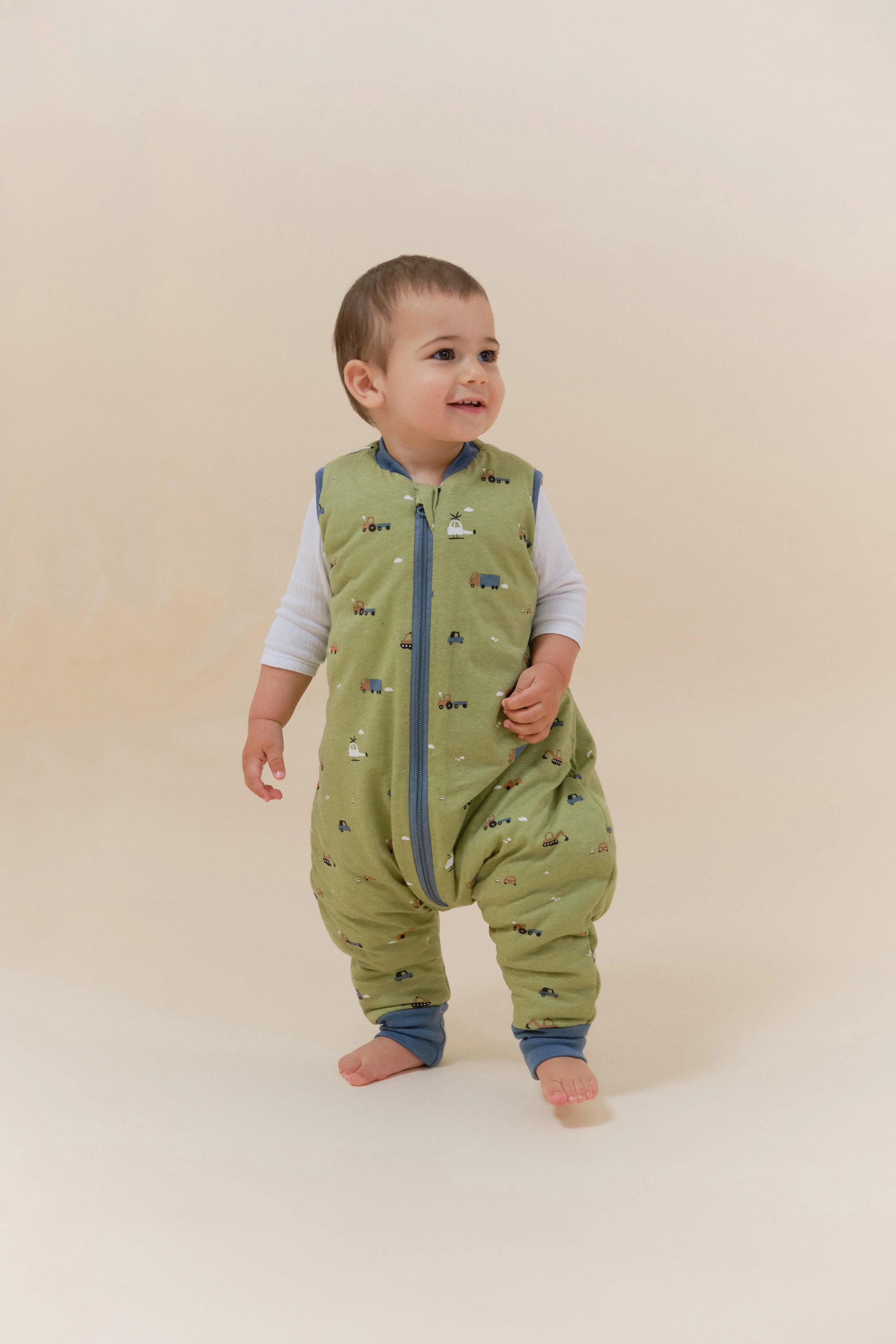 Bebé feliz a usar o saco de dormir MolisandCo TOG 2.5 com pés, padrão Little Drivers, para liberdade de movimento.