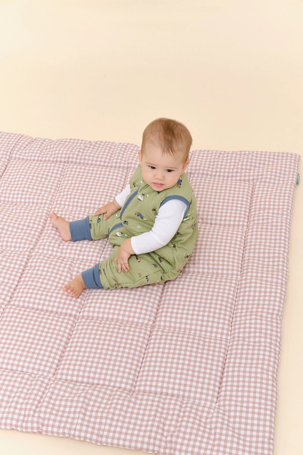 Bebé sentado confortavelmente no saco de dormir MolisandCo TOG 2.5 com pés Little Drivers, sobre manta xadrez.