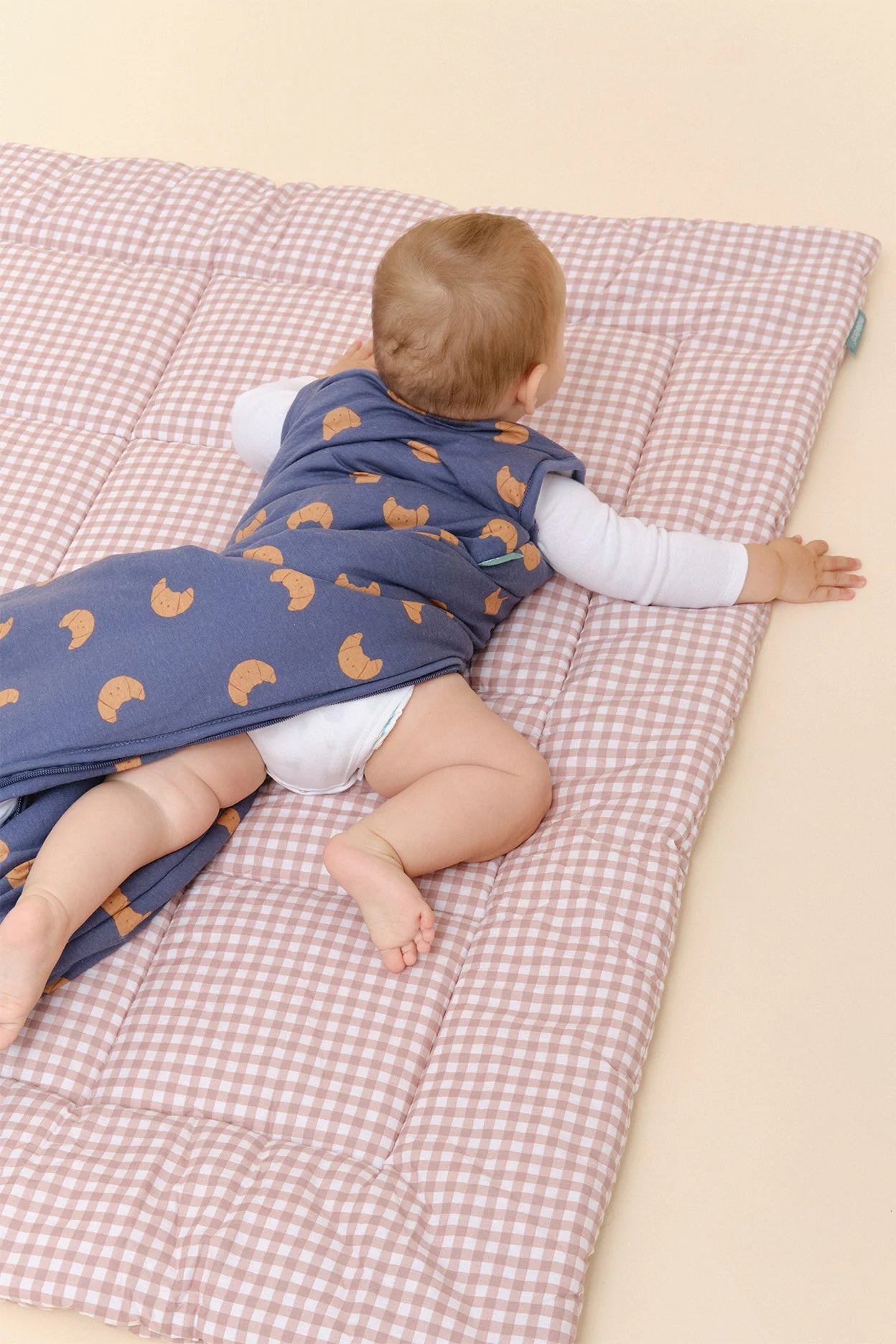 Bebé deitado de bruços, com saco de dormir MolisandCo TOG 2.5 azul de croissants, mostrando liberdade de movimento.