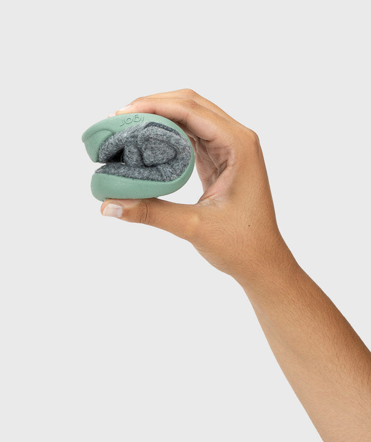 Pantufa dobrada na mão, demonstrando a sua flexibilidade extrema, essencial para respeitar a mobilidade natural dos pés e promover um desenvolvimento saudável.