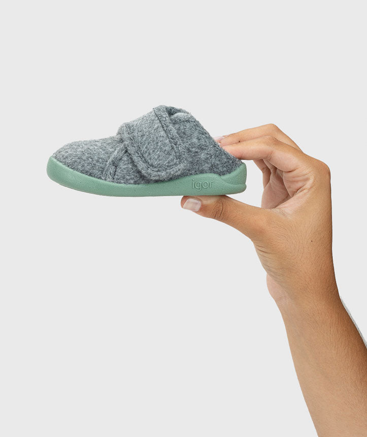 Pantufa segurada na mão, evidenciando a sua leveza e flexibilidade, garantindo um ajuste natural e confortável para os pés das crianças.