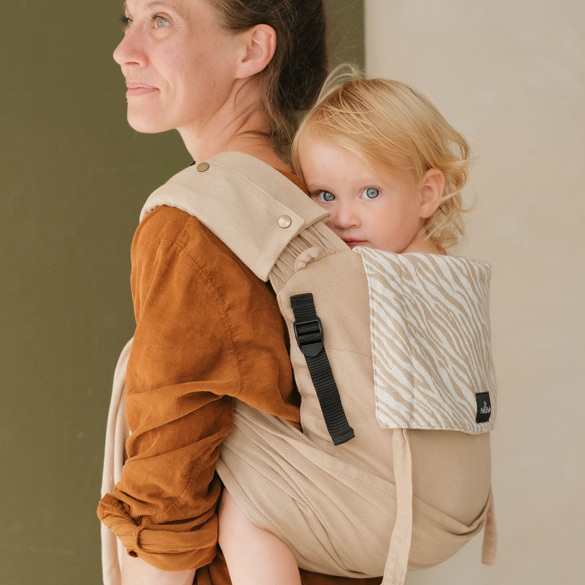 Close-up de uma mãe a carregar o bebé, focando nos detalhes do tecido e ajuste do Mei Tai Evolutivo Neobulle P'tit Evo Savane.