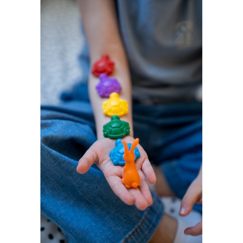 Mão de uma criança segurando as peças magnéticas do SmartGames Turtle Tactics (tartarugas e lebre), mostrando as cores vibrantes das peças.