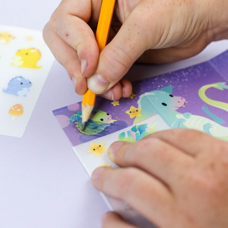 Mãos de uma criança a usar o lápis para transferir um autocolante de um dragão para o cenário.