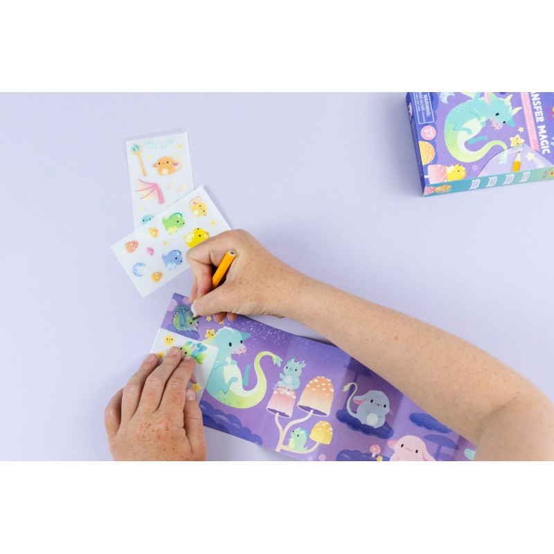 Mãos de uma pessoa a usar o lápis para transferir um autocolante para o cenário dobrável, mostrando o processo de transferência e o resultado final.