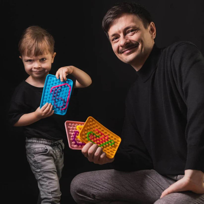 Um pai e um filho com os seus Wiggly Toy Jogos Sensoriais, o filho a segurar um tabuleiro azul e o pai a exibir dois tabuleiros, um rosa e um laranja, com padrões criados.