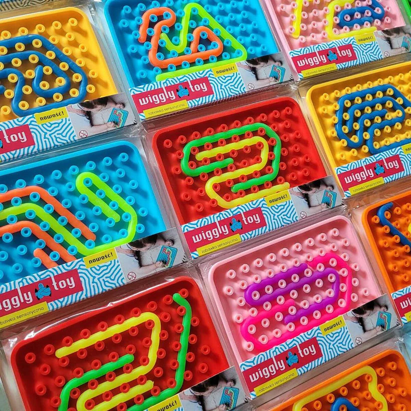 Múltiplos conjuntos do Wiggly Toy Jogo Sensorial em várias cores vibrantes, exibindo as bases e as peças flexíveis em diferentes padrões, ainda nas suas embalagens de plástico.