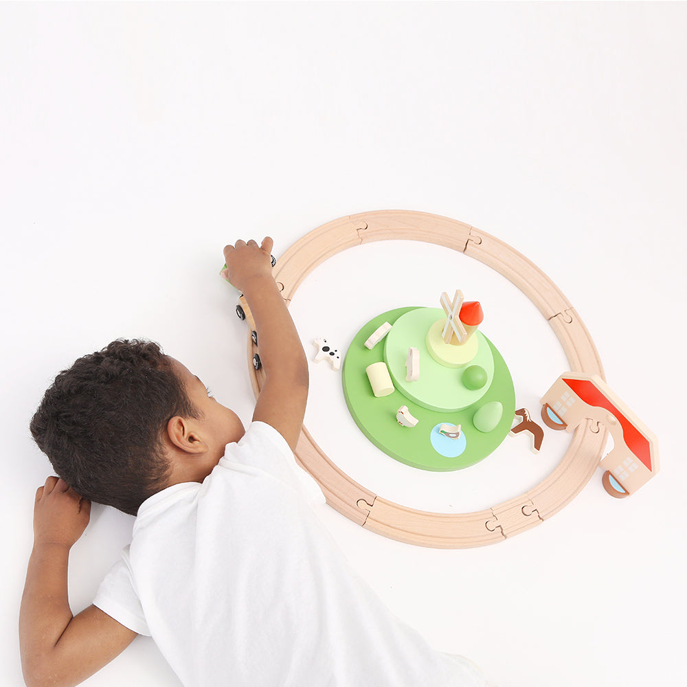 Vista de cima de uma criança a brincar com o comboio de madeira Classic World, mostrando a disposição da pista e dos elementos da quinta.