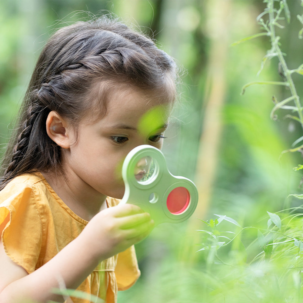 Menina explorando a natureza com a lupa de madeira Classic World Lupa e Prismas Visuais.