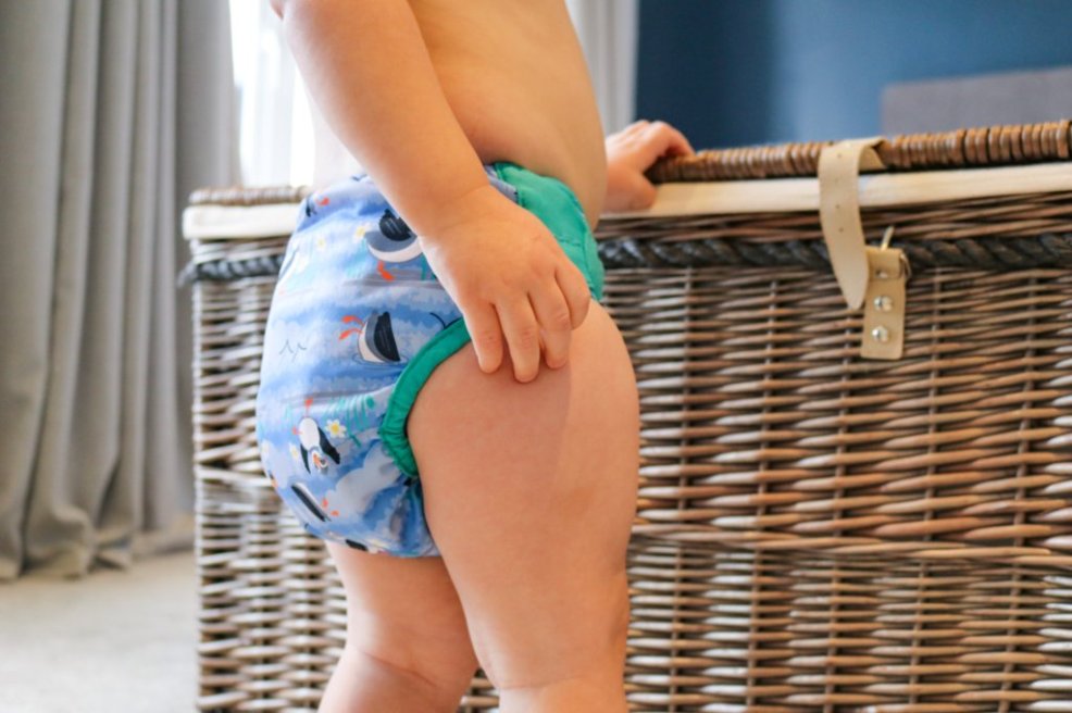 Bebé a usar a fralda reutilizável Close Pop-in, de pé (vista lateral).