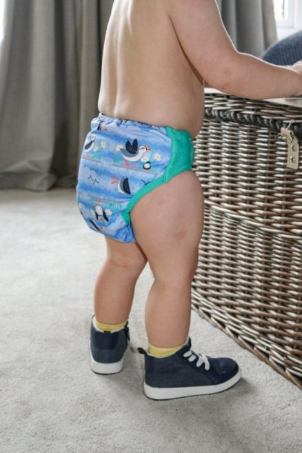 Bebé a usar a fralda reutilizável Close Pop-in, de pé (vista traseira).