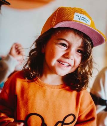 Criança sorridente a usar o chapéu de pala/boné Hello Hossy PANA amarelo 2-5 anos.