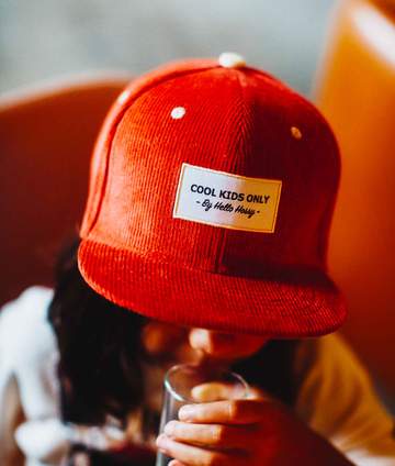 Criança a usar o chapéu de pala/boné Hello Hossy PANA vermelho 2-5 anos com etiqueta "Cool Kids Only".