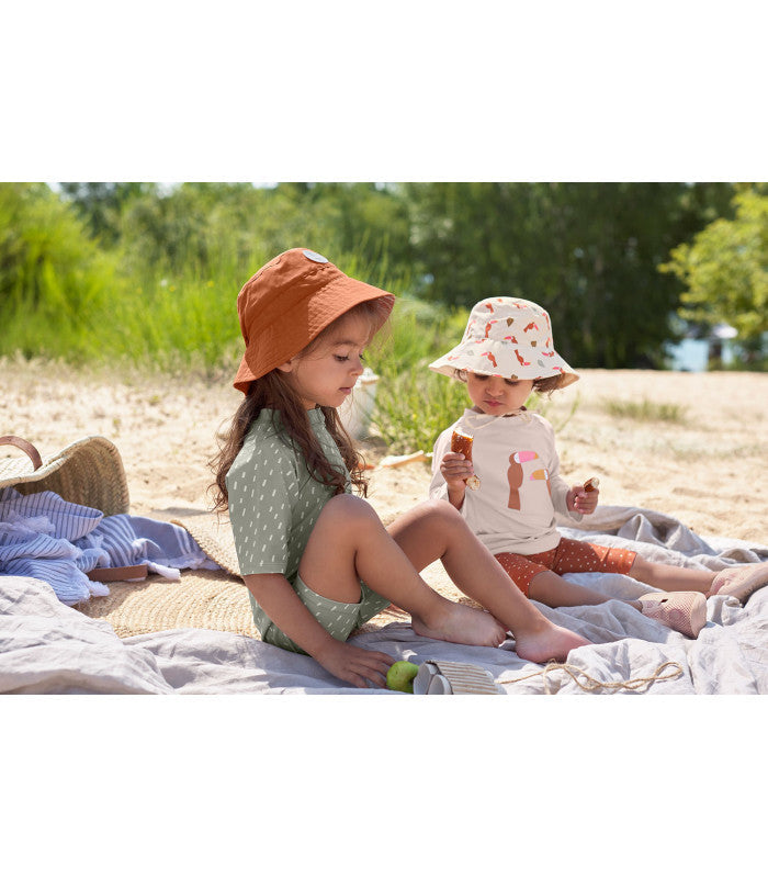 Crianças na praia com chapéus Lassig, mostrando o uso de proteção solar para bebés e crianças.