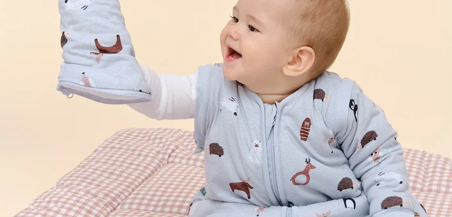 Bebé num saco de dormir com mangas, a brincar com as mãos