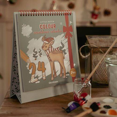 Calendário do Advento Little Dutch X-mas aberto sobre uma mesa, com tintas e pincéis, pronto para ser colorido