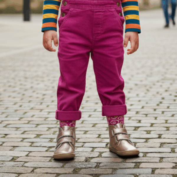 Criança em pé, a usar as botas Baby Lobitos Barefoot Bota Afrodita cor bronze com meias, em rua de calçada.