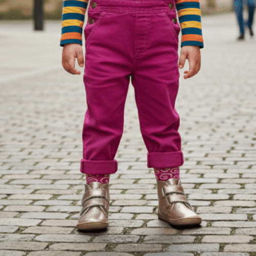 Criança em pé, a usar as botas Baby Lobitos Barefoot Bota Afrodita cor bronze com meias, em rua de calçada.