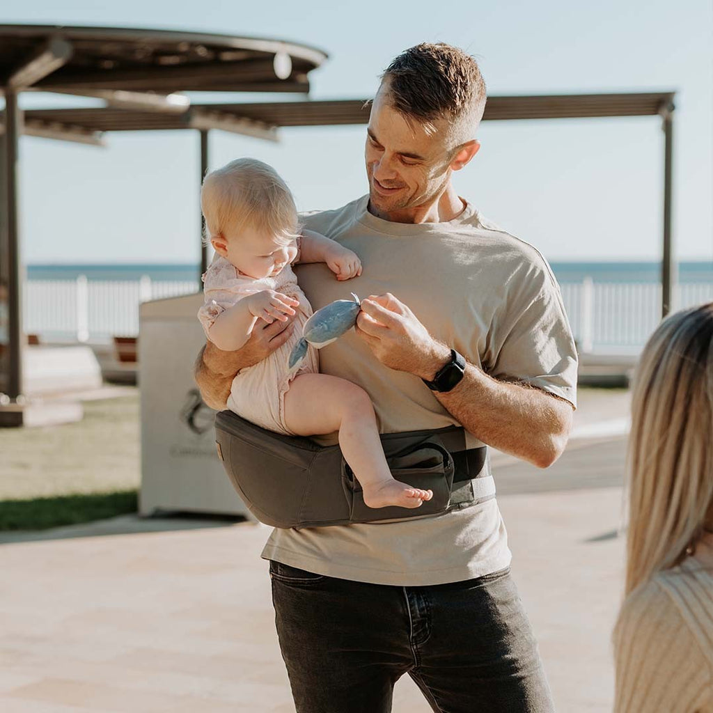 Hip Seat Quokkababy verde sage em uso, com a criança sentada na anca