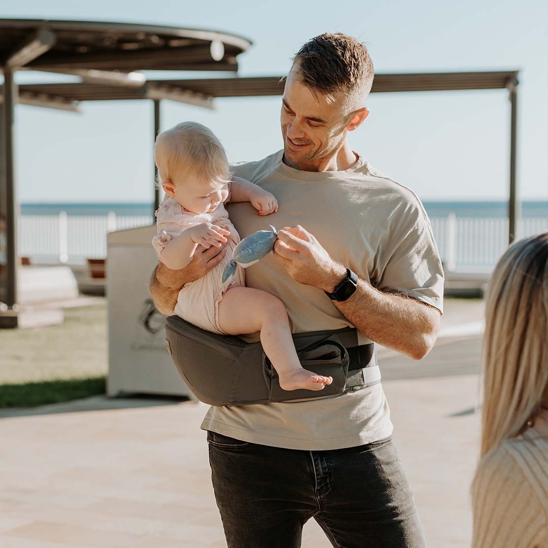 Hip Seat Quokkababy verde sage em uso, com a criança sentada na anca