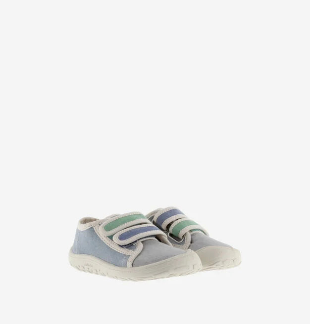 Par de sapatilhas infantis de lona, azul e cinzenta, com detalhes em verde e azul nas tiras de velcro, colocadas lado a lado em fundo branco.