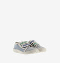 Par de sapatilhas infantis de lona, azul e cinzenta, com detalhes em verde e azul nas tiras de velcro, colocadas lado a lado em fundo branco.