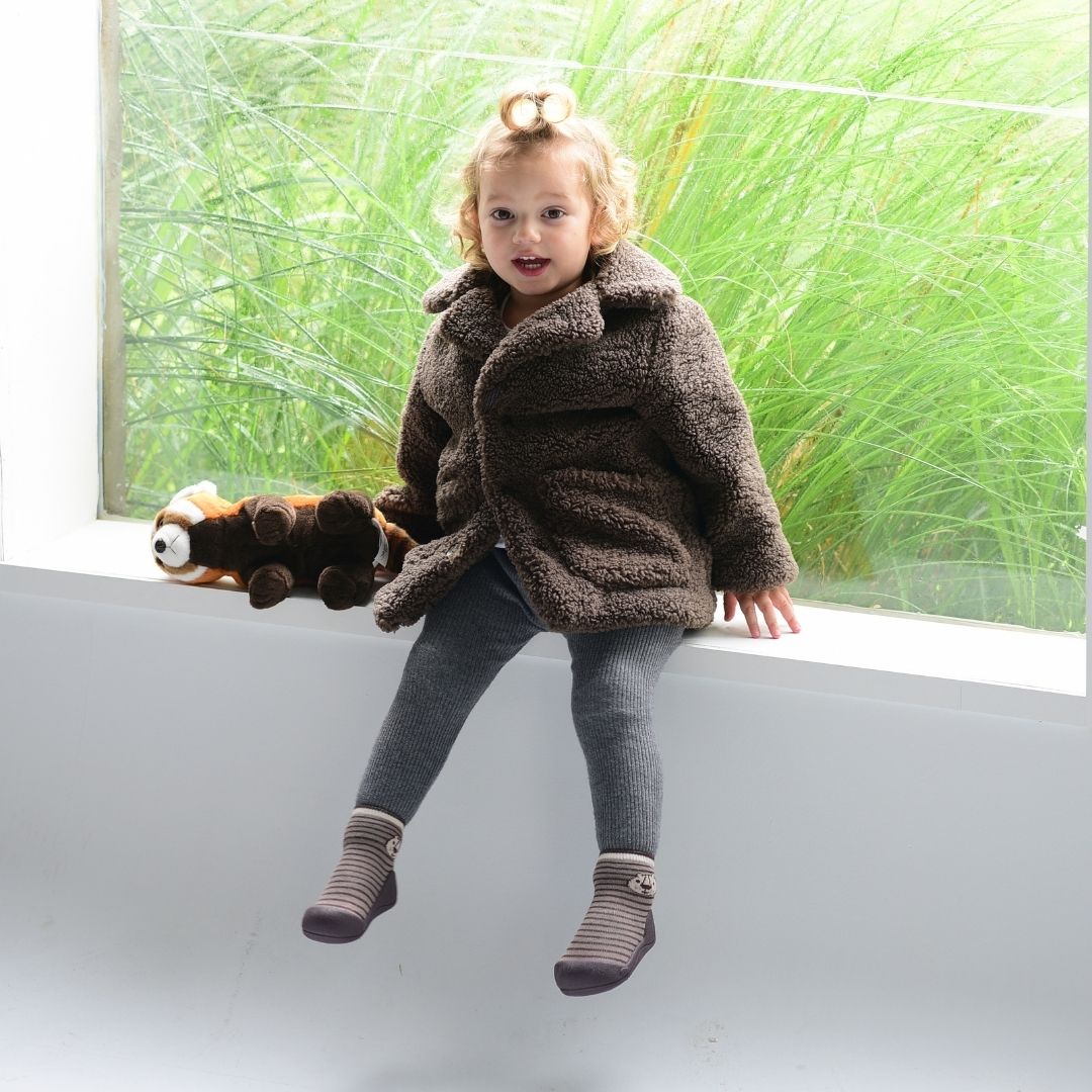 Criança sentada junto à janela a usar os sapatos-meia Attipas Forest Khaki.