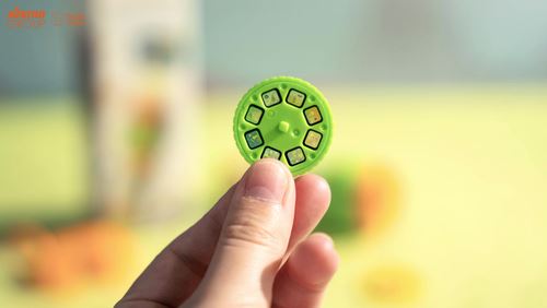 Mão a segurar um dos discos de filme verdes do projetor, mostrando as pequenas imagens quadradas que serão projetadas.