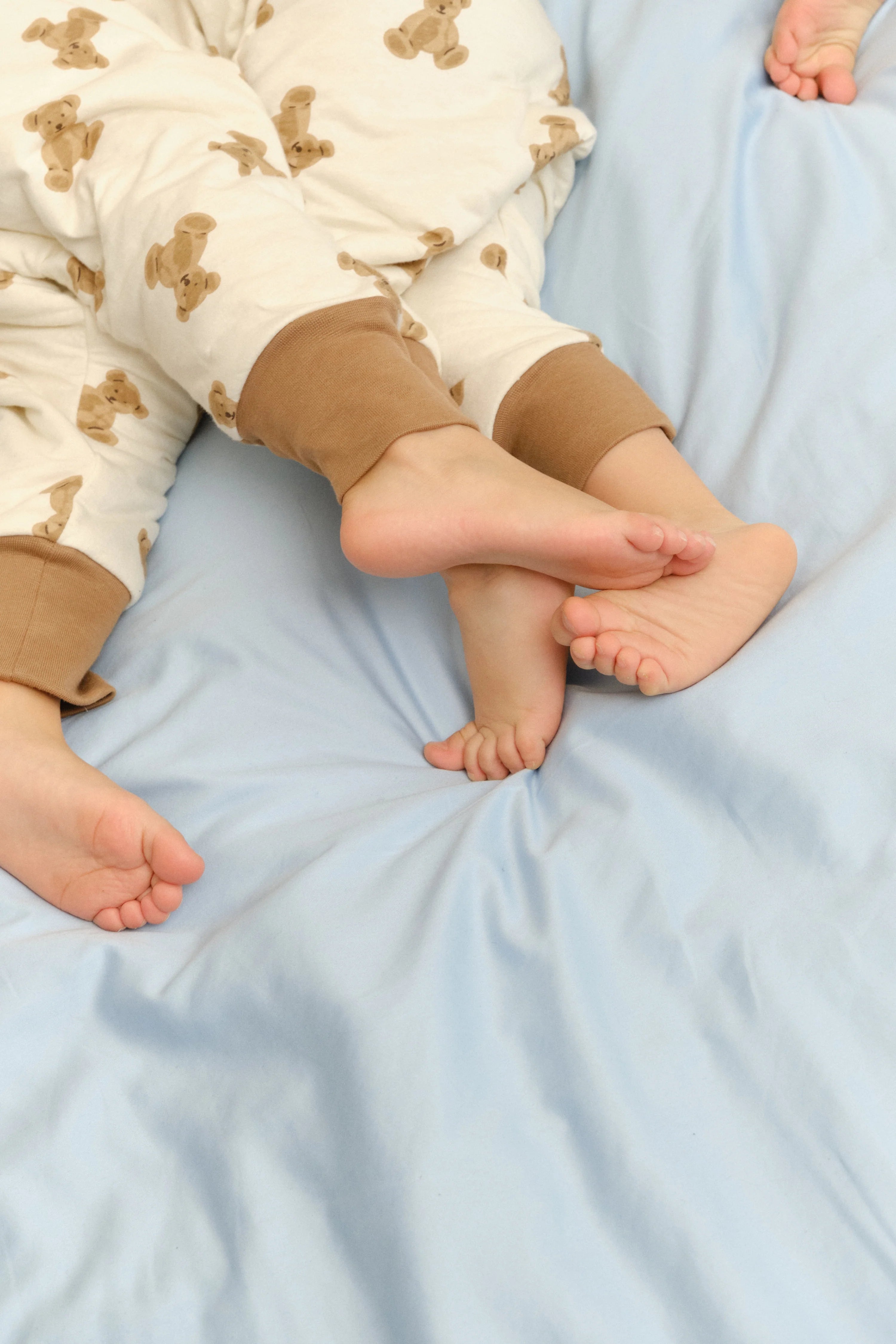 Pés de duas crianças na cama, uma com o saco de dormir MolisandCo TOG 1.0 [TEDDY] e outra com os pés descalços, mostrando a liberdade de movimento.