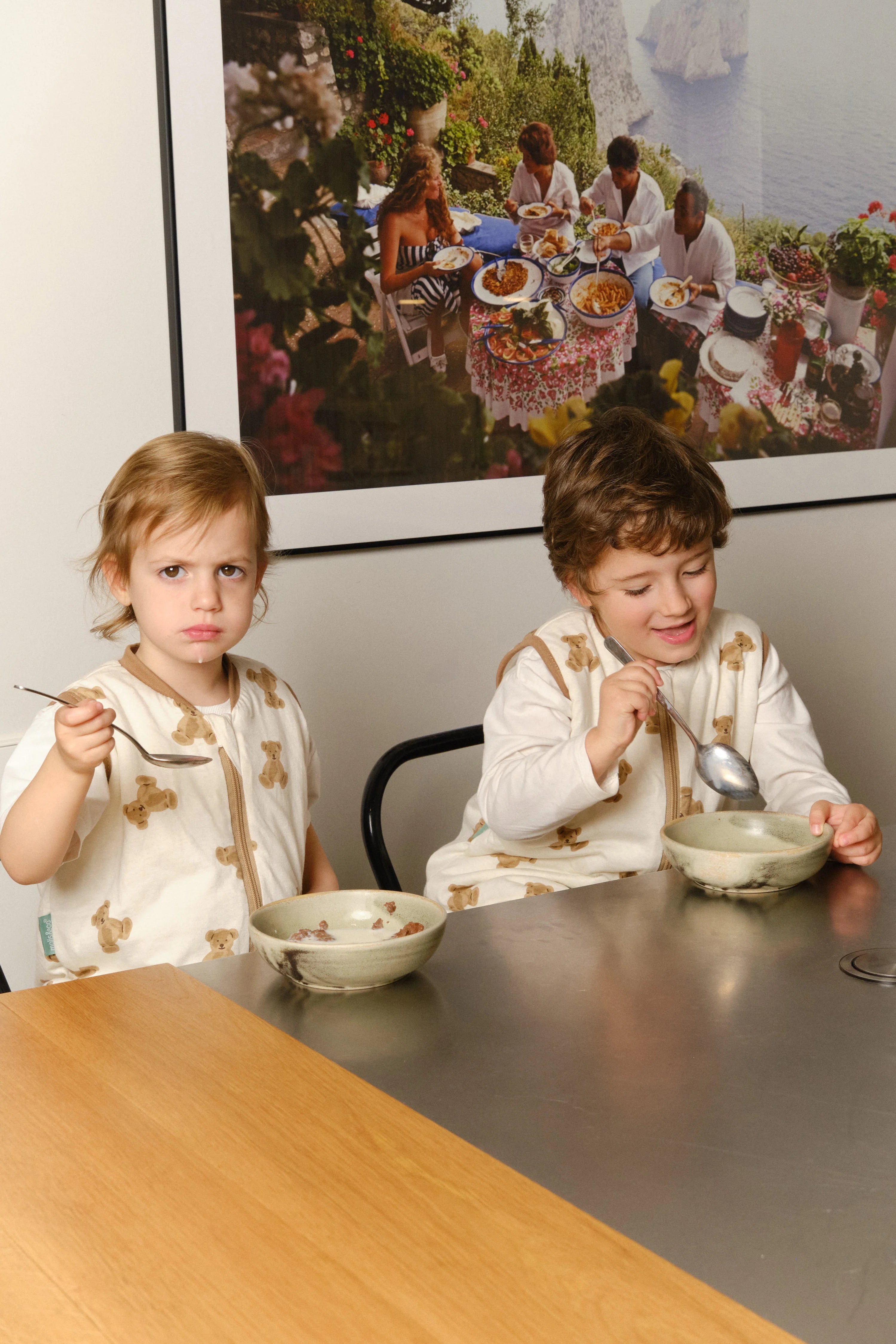 Duas crianças sentadas à mesa a comer, ambas a usar o saco de dormir MolisandCo TOG 1.0 [TEDDY], mostrando a sua versatilidade para atividades.