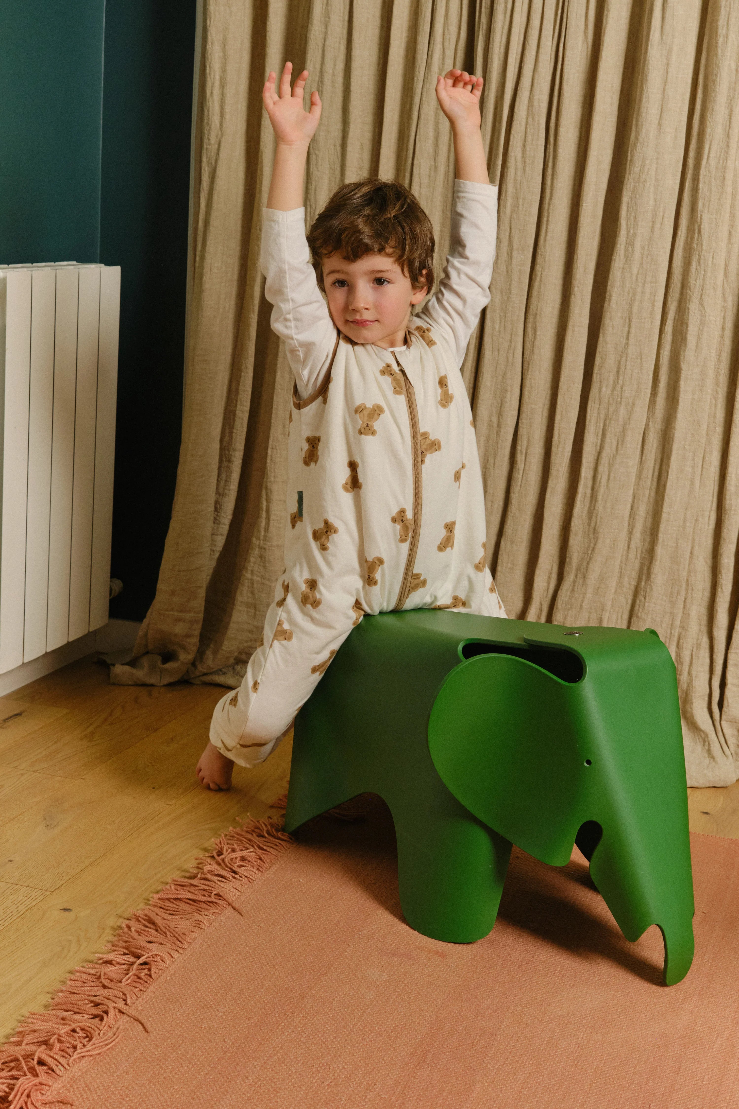 Criança sentada num banco em forma de elefante, a usar o saco de dormir MolisandCo TOG 1.0 [TEDDY] com os braços levantados, evidenciando a liberdade de movimentos.