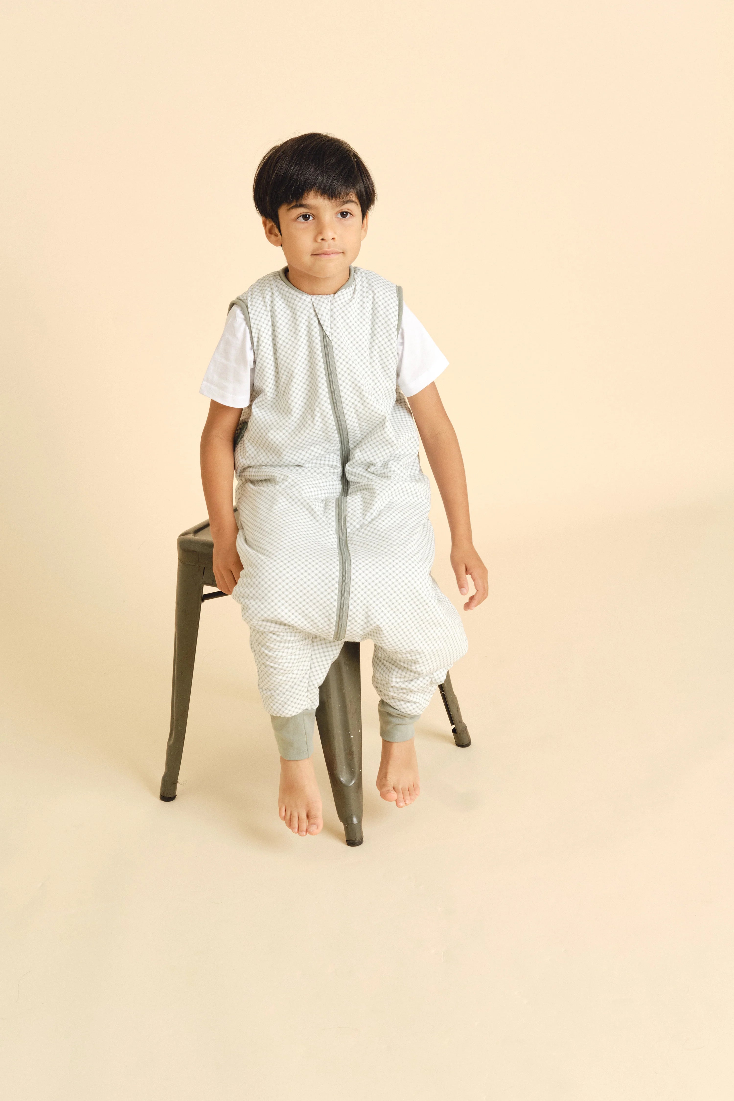 Criança sentada num banco, vestindo o saco de dormir MolisandCo TOG 1.0 com pés VICHY GREEN, demonstrando conforto e mobilidade.