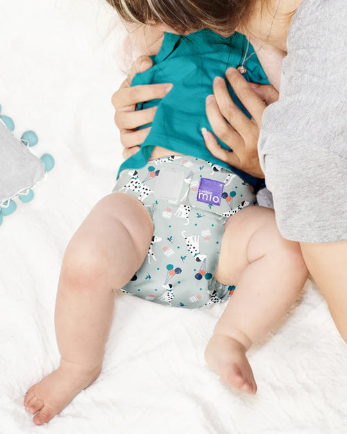 Bebé deitado a ser amamentado, a usar uma fralda reutilizável Bambino Mio miosolo classic com padrão de dálmatas e balões.