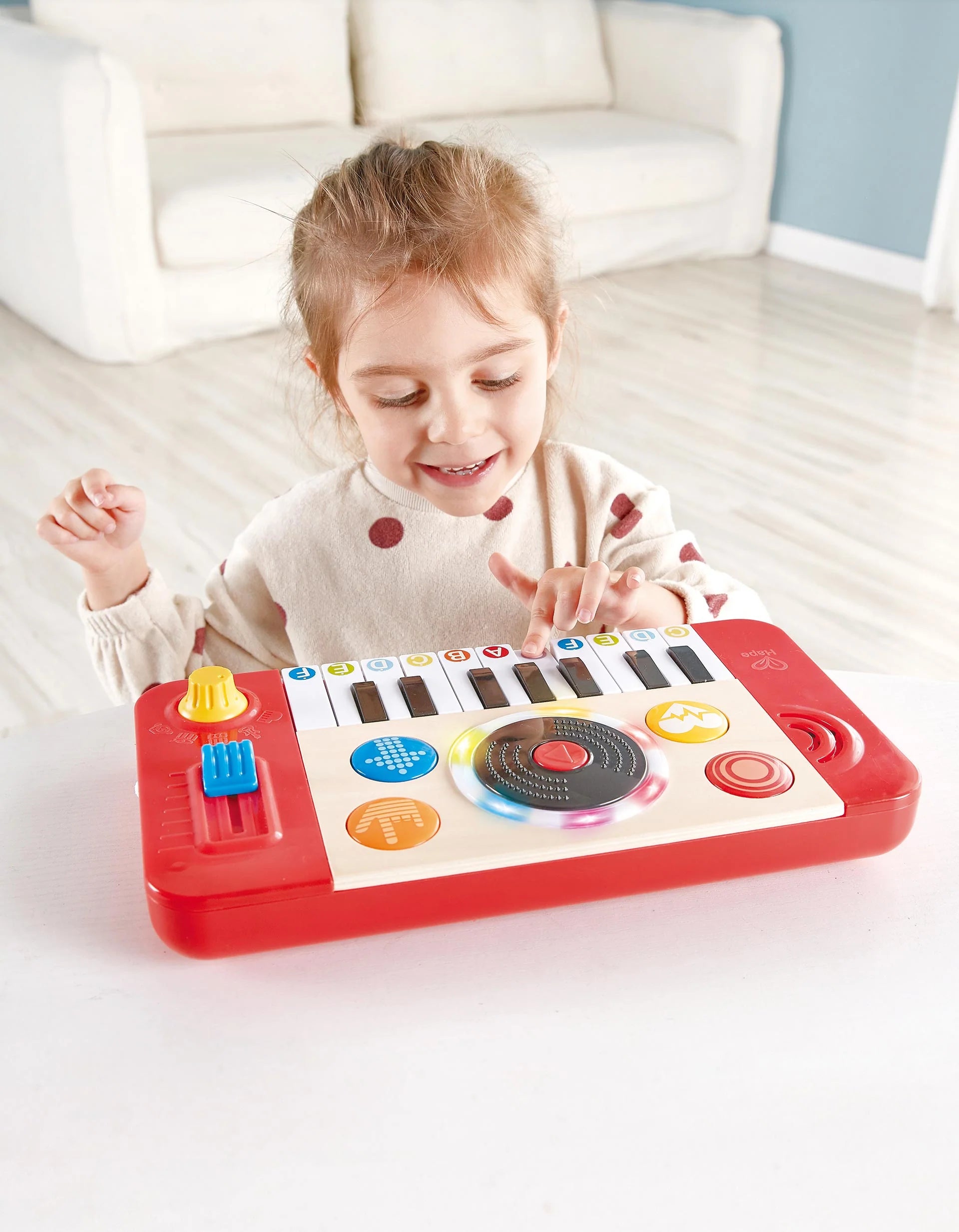 Criança sorridente a interagir com o Hape Estúdio de DJ e mesa de mistura, explorando as teclas e o disco.