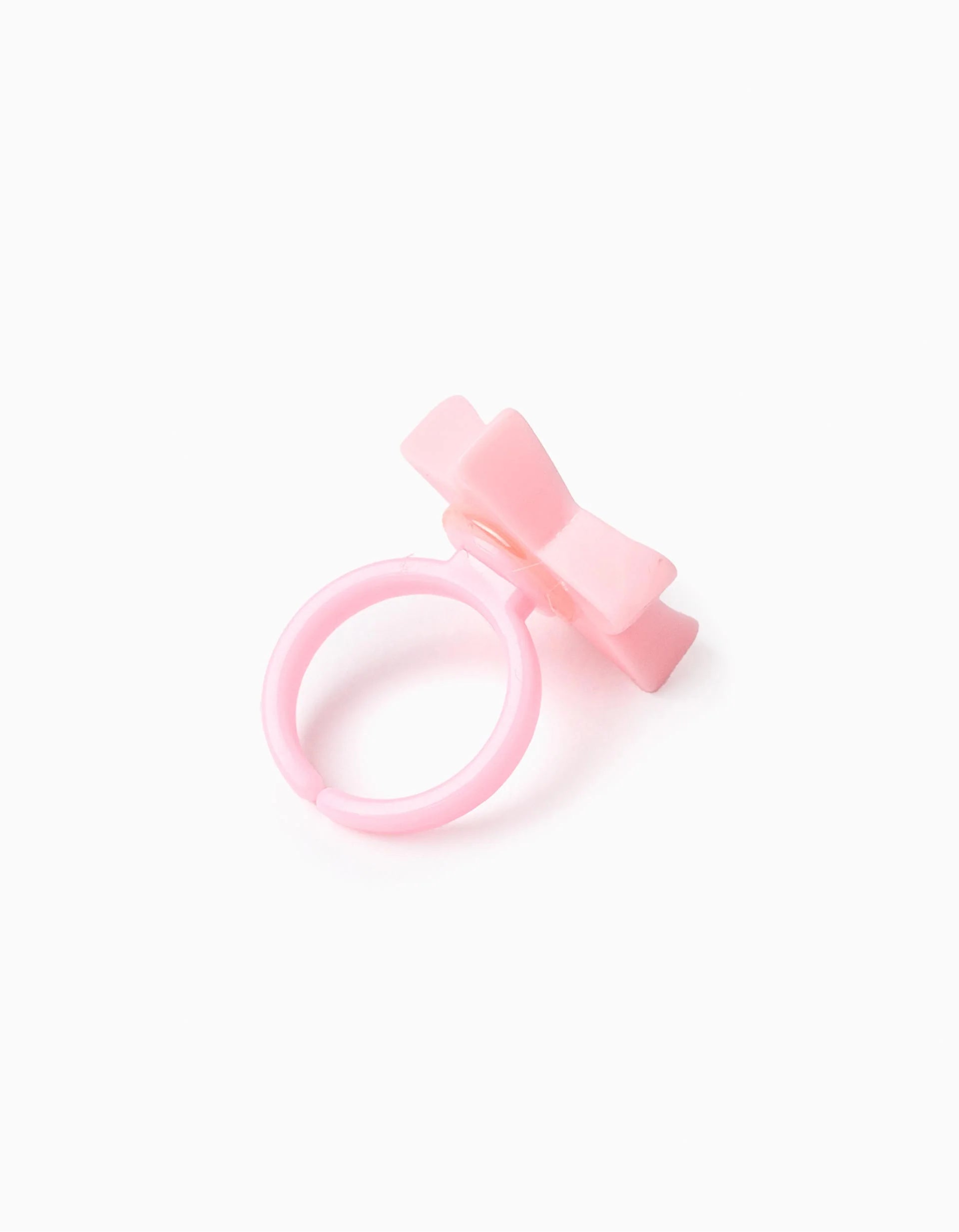 Detalhe de um anel cor-de-rosa em forma de laço, acessório que acompanha o Lip Gloss Sweet, sobre fundo branco.