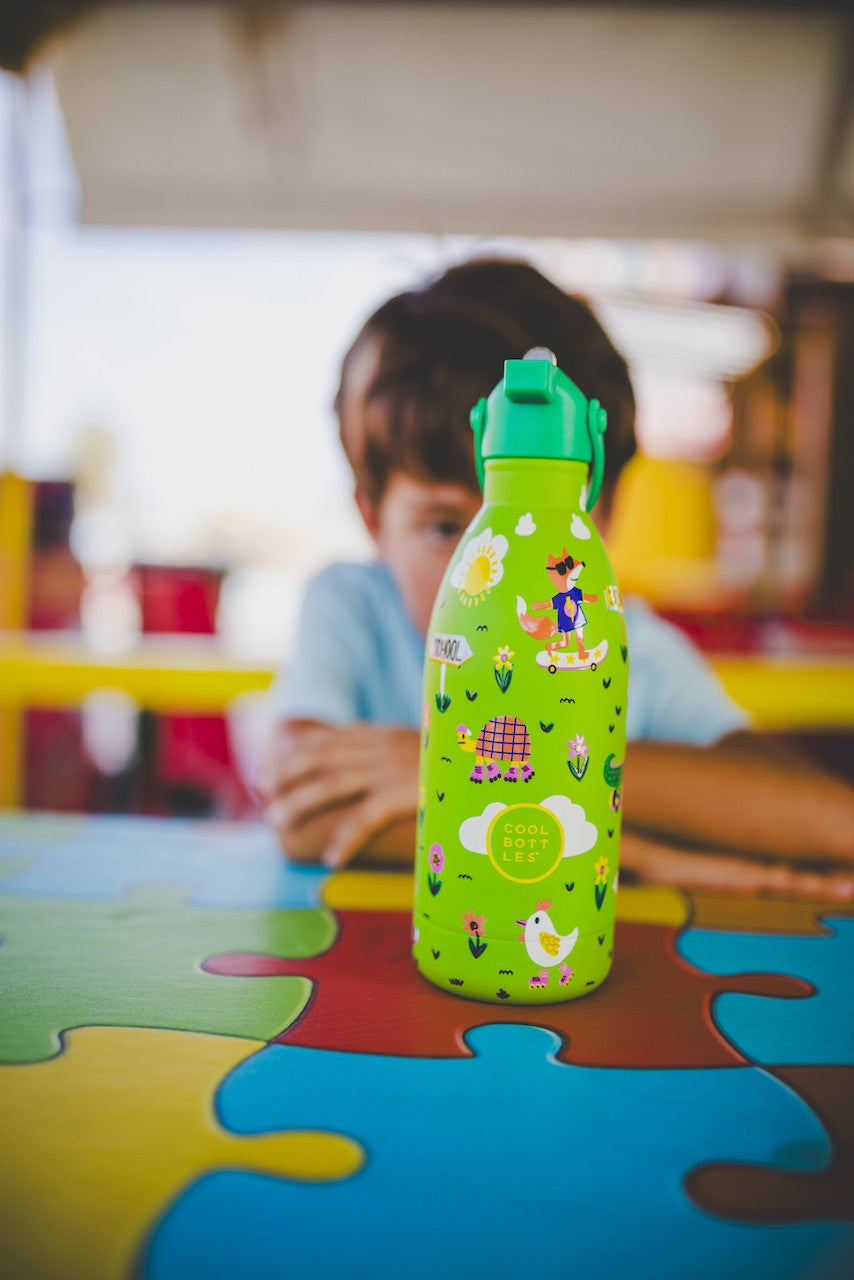 Criança sentada à mesa com a garrafa térmica Cool Bottles Rolling Skaters 500ml em primeiro plano.