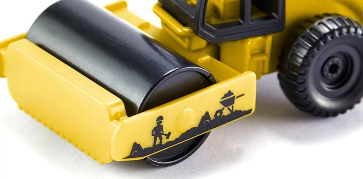 Close-up do rolo compactador miniatura SIKU amarelo, focando no rolo preto e nos detalhes da silhueta de trabalhadores na estrutura frontal.