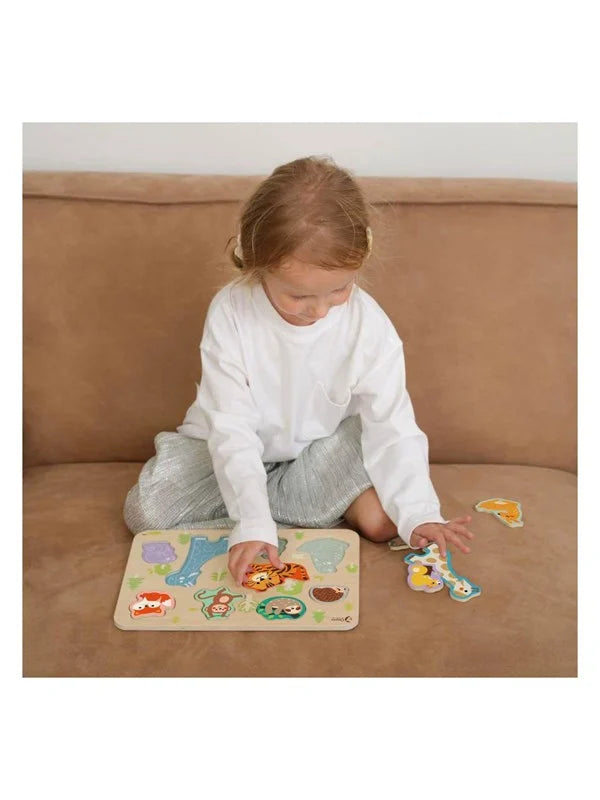 Criança sentada num sofá a brincar com o Classic World Puzzle de encaixe Animais de madeira, com várias peças espalhadas.