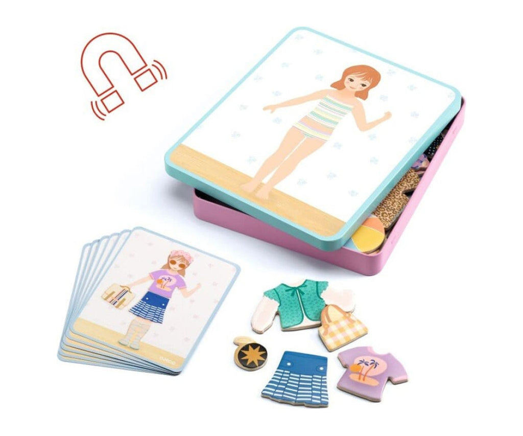 Vista geral do conteúdo do jogo: caixa metálica aberta, cartas modelo e peças de roupa magnéticas de madeira espalhadas.