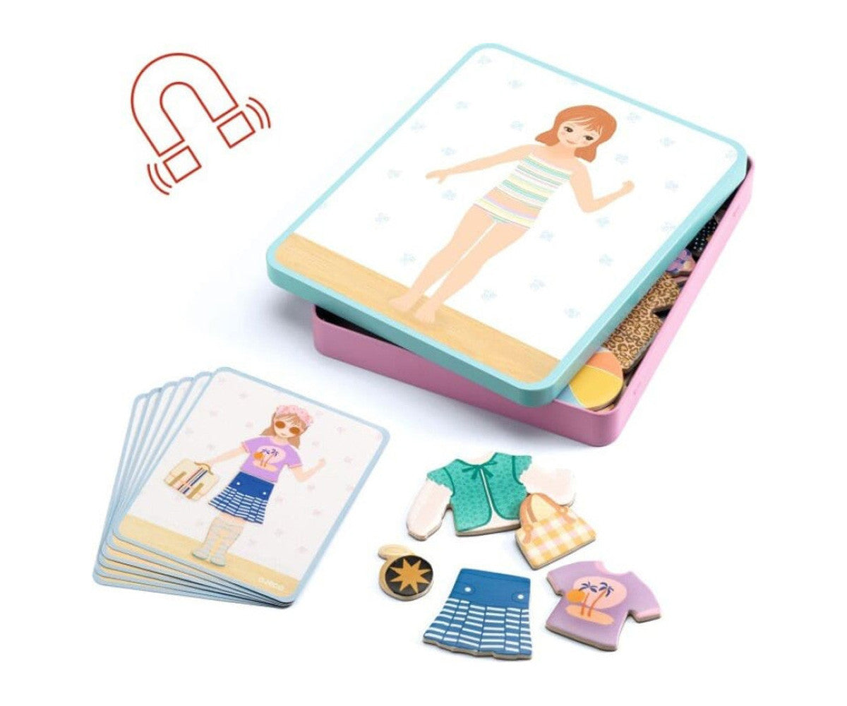 Vista geral do conteúdo do jogo: caixa metálica aberta, cartas modelo e peças de roupa magnéticas de madeira espalhadas.