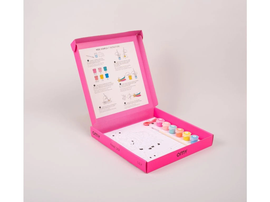 Interior da caixa OMY Lily mostrando as tintas, pincel e cartões para colorir, com instruções ilustradas na tampa.