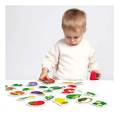 Uma criança pequena sentada a brincar com os puzzles de frutas e vegetais da Banana Panda numa superfície branca, concentrada a encaixar uma peça.