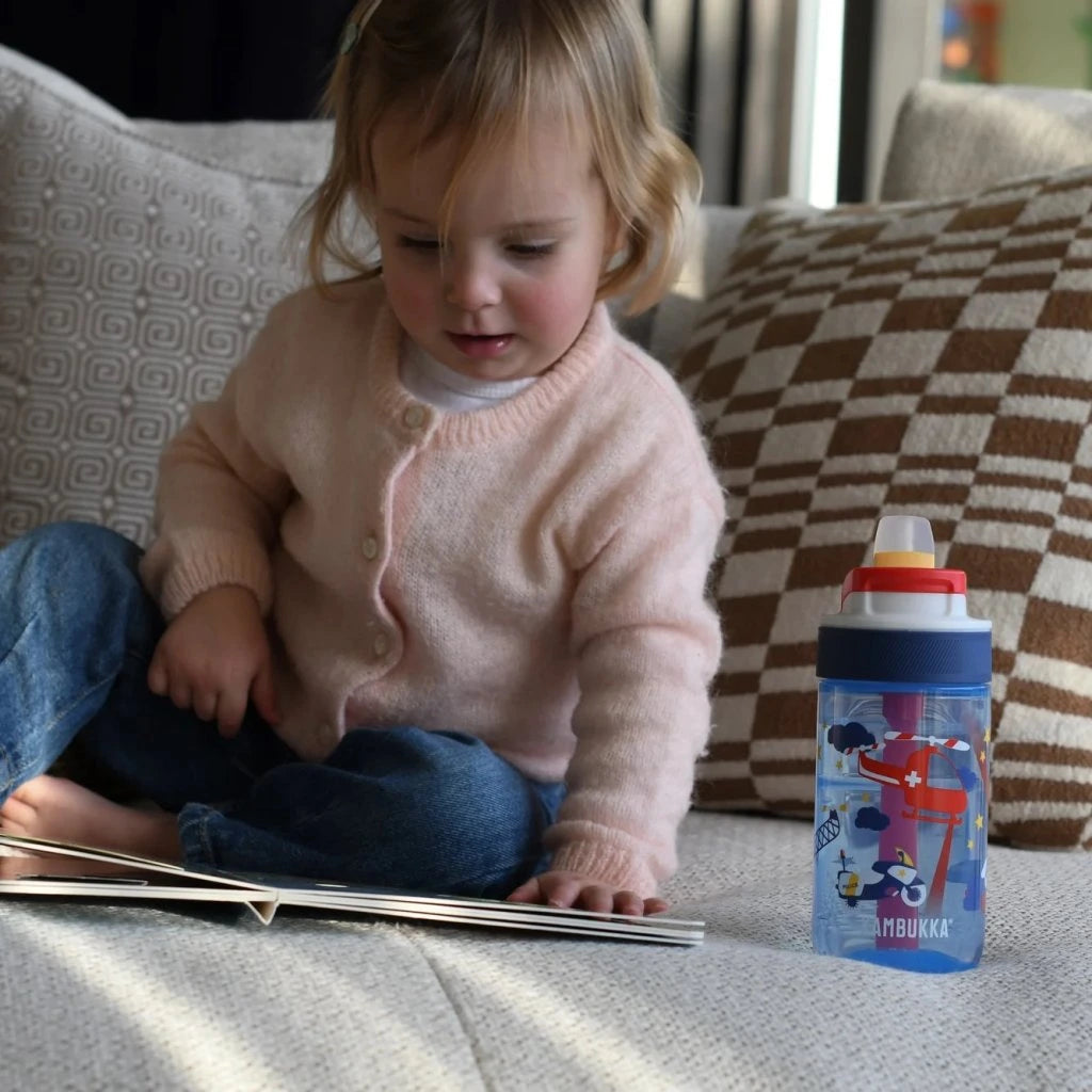 Uma menina sentada no sofá a ler um livro, com uma garrafa Kambukka LAGOON Police Patrol 400 ml ao seu lado.