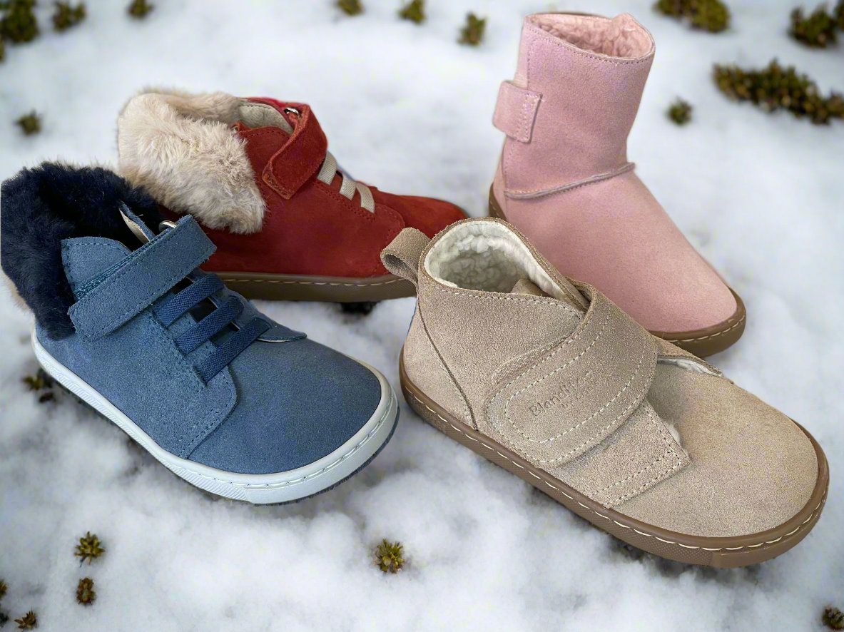 Quatro pares de calçado infantil barefoot para outono/inverno, dispostos sobre uma superfície de neve. Os modelos incluem botinhas de cores azul, vermelho, bege e rosa, com solas flexíveis e detalhes em pelo, perfeitos para manter os pés das crianças quentes e confortáveis.